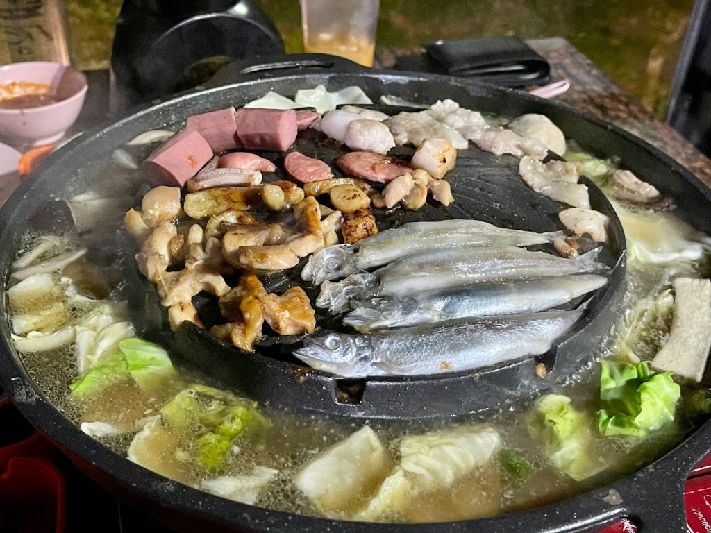 cheap Mookata with fish, sausages and lean shabu shabu meat slices grilling on plate